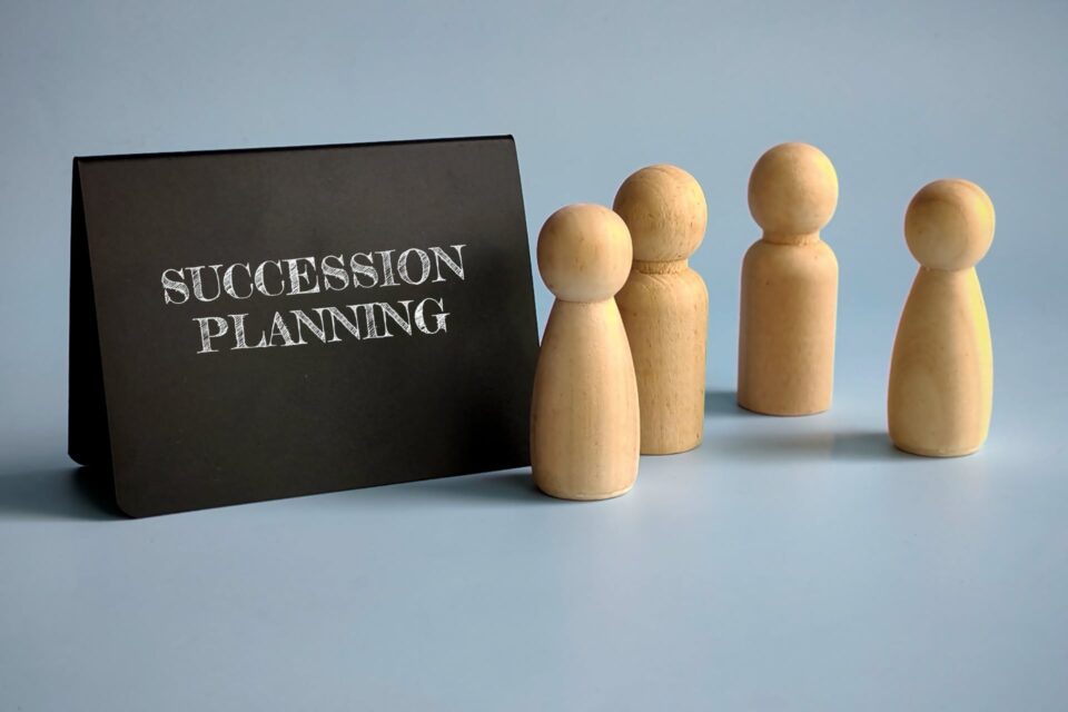 Black succession planning sign with wooden peg figures on a gray surface
