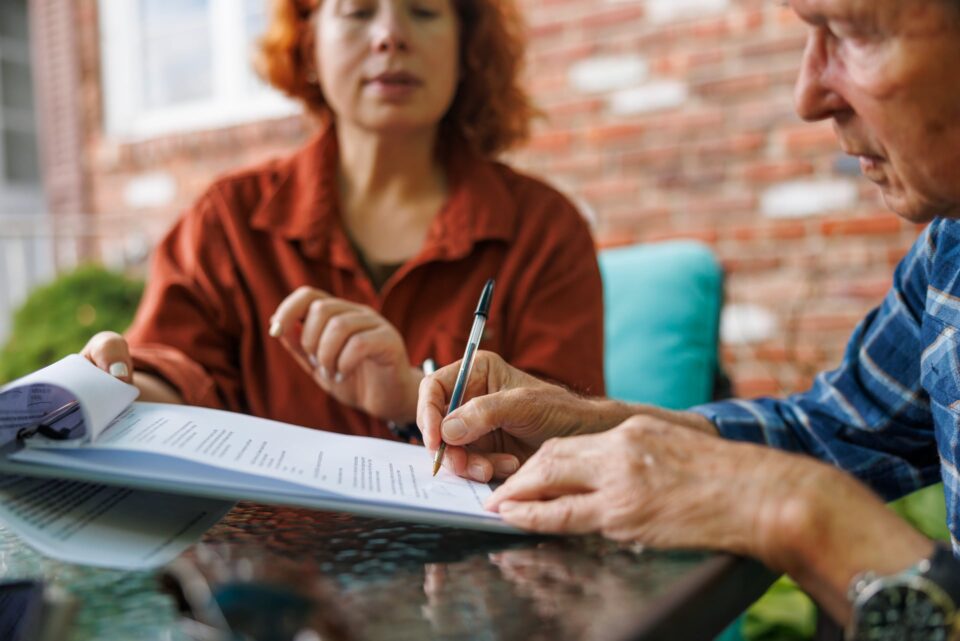 Woman with red hair leaning across a table to watch a man sign a document