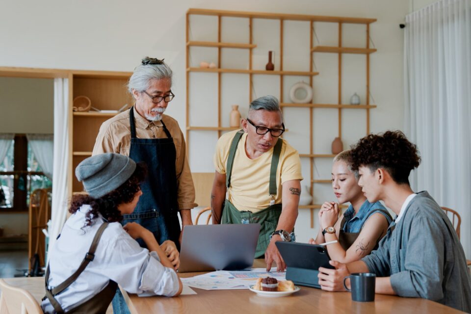 Three generations of a family gathered around a laptop in a warm workshop space