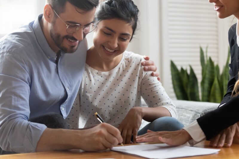 Couple smiling while signing a document as a third person looks on