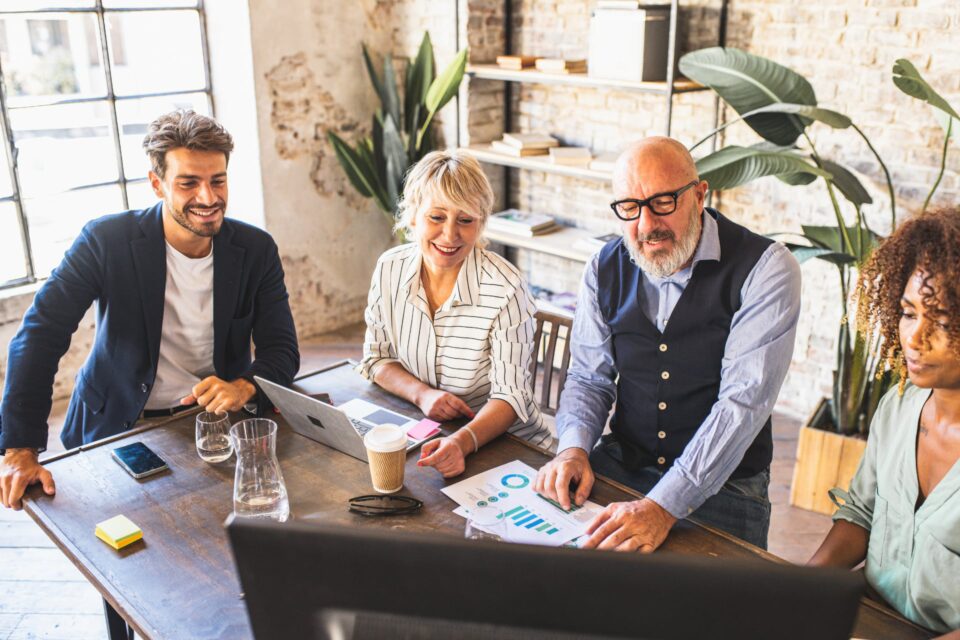 Four colleagues gathered around a laptop in a bright modern office