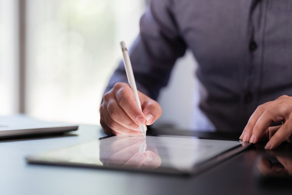 Person in a suit signing a document with a stylus on a tablet at a dark desk