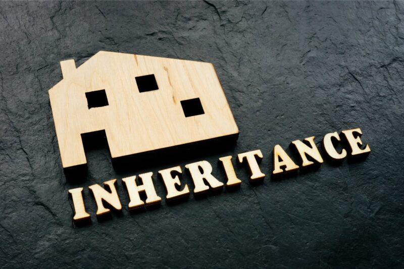 Two wooden house shapes with the word INHERITANCE spelled out in gold letters on a dark background