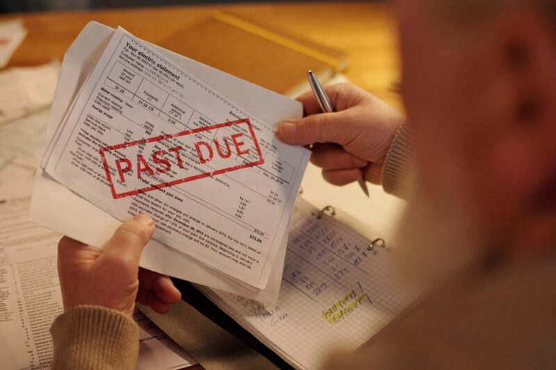 Hand holding a bill stamped PAST DUE in red over a notebook with handwritten entries