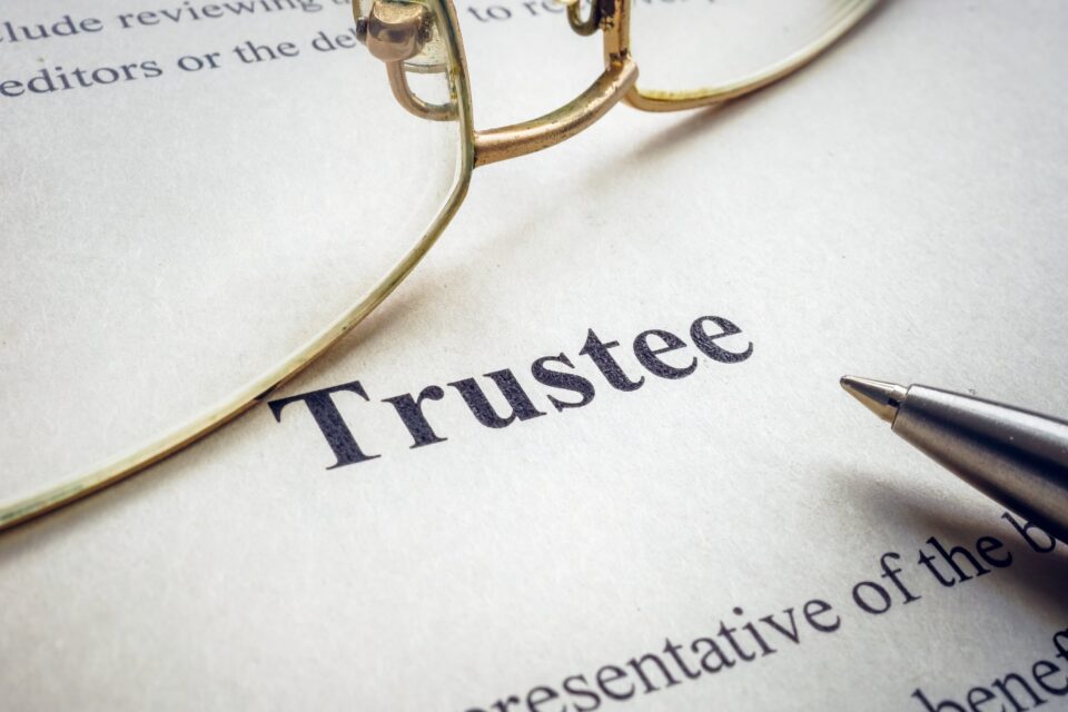 Close-up of the word Trustee on a printed legal document with glasses and a pen