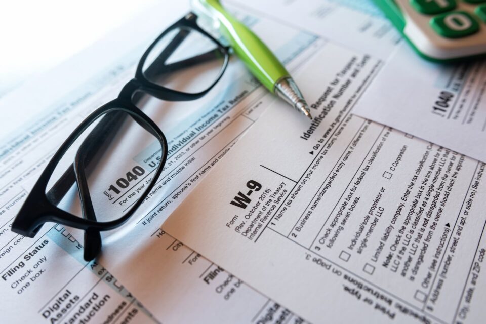 Reading glasses and green pen resting on IRS tax forms including a W-9