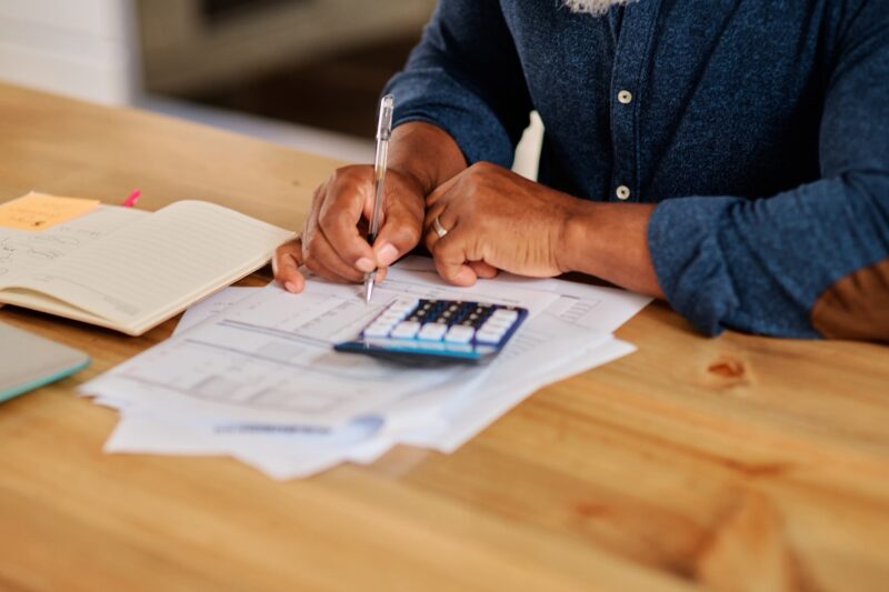 Older person seated at a table with documents and a calculator, writing