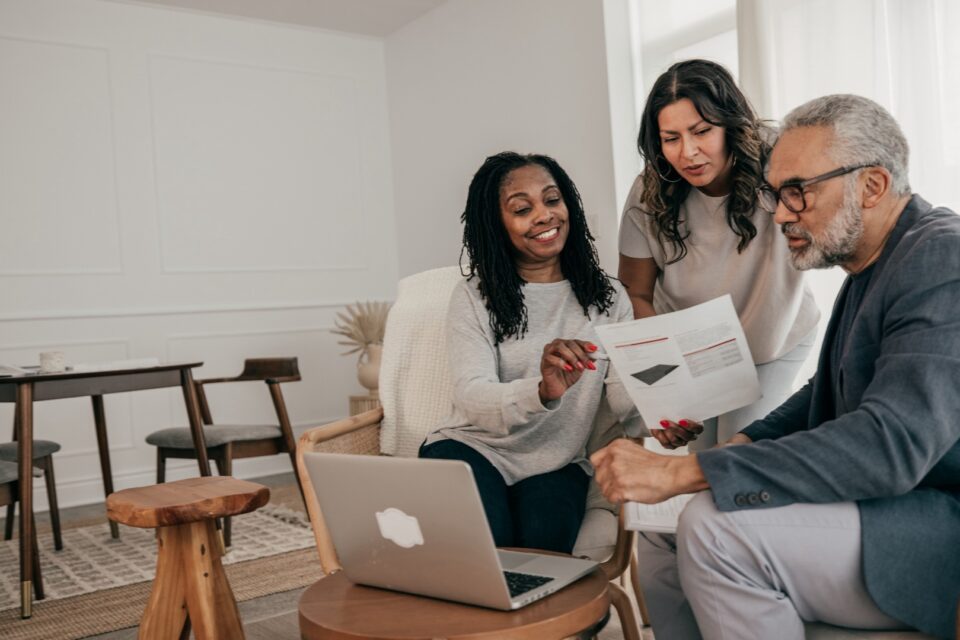 Man and woman sitting across from another person, reviewing papers with a laptop