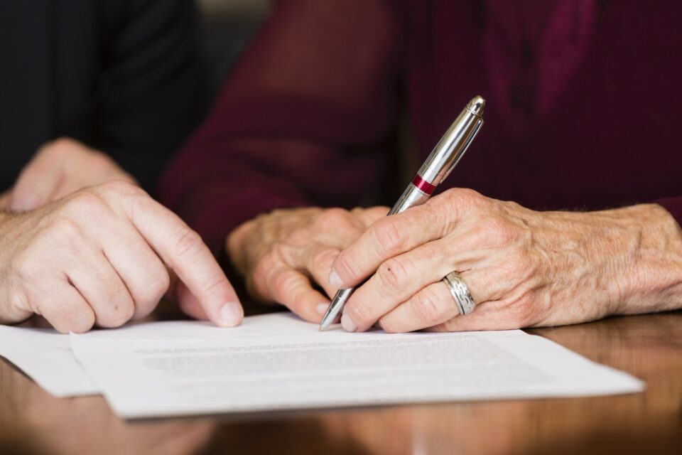 Elderly hands holding a pen, signing a document