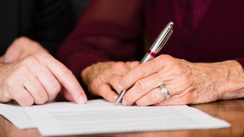 Close-up of a hand signing a document with a pen, wearing a ring
