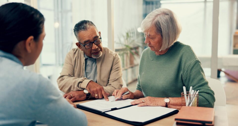 Three people at a table with documents, two older adults and a younger woman