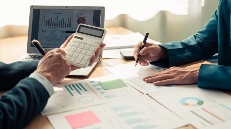 Person at a desk reviewing financial charts with a calculator and pen